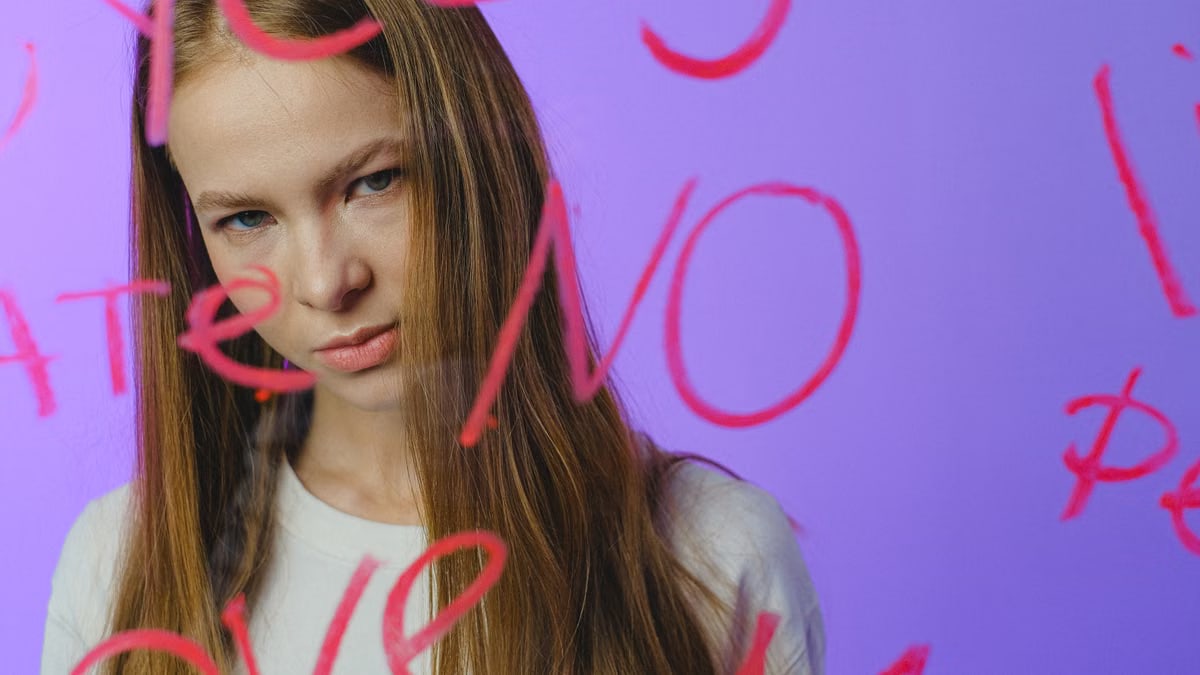 Teen girl with thoughtful expression behind written glass, moody studio shot.